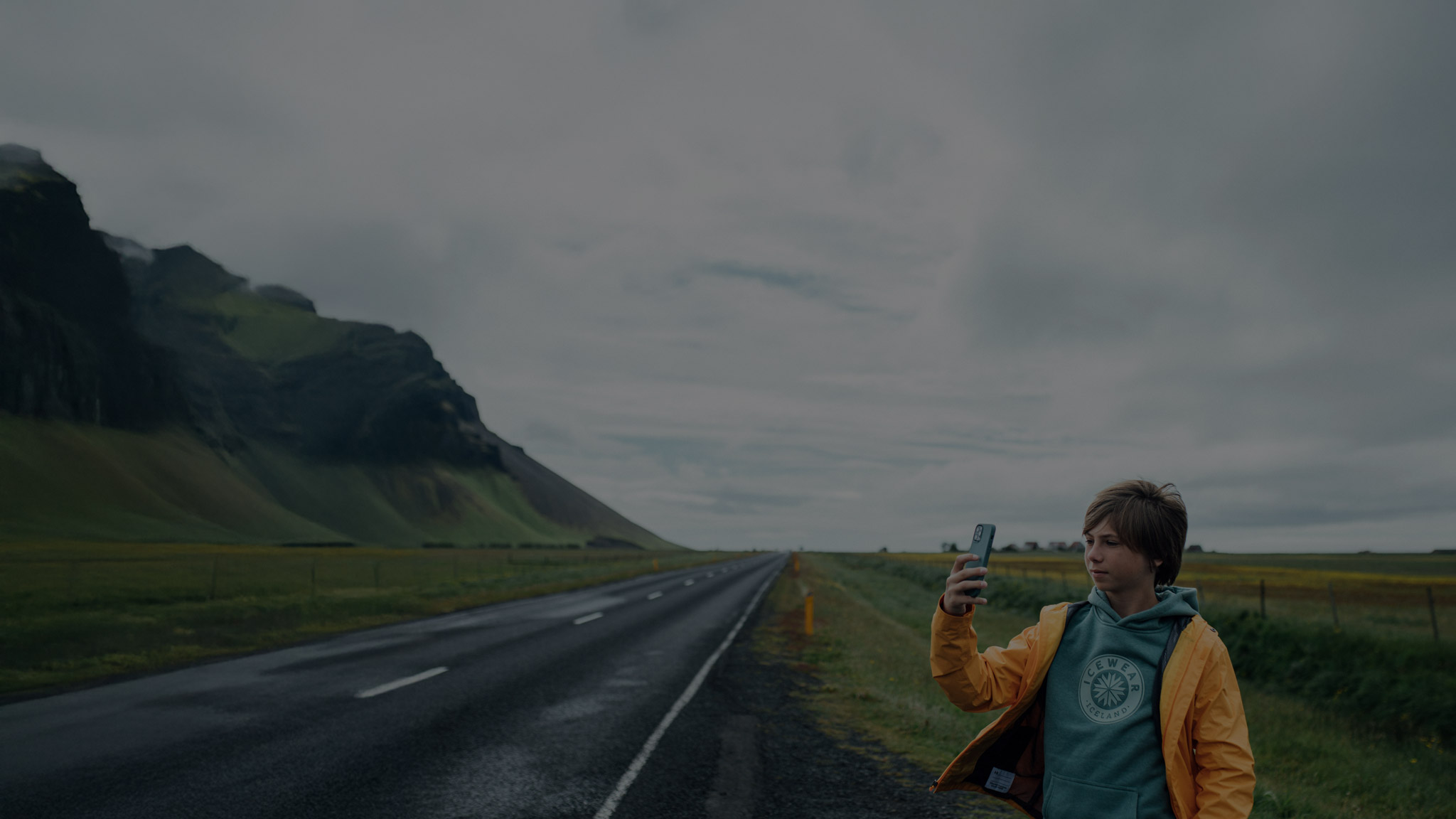 Photo of Icelandic landscape, a boy taking a picture next to a street.