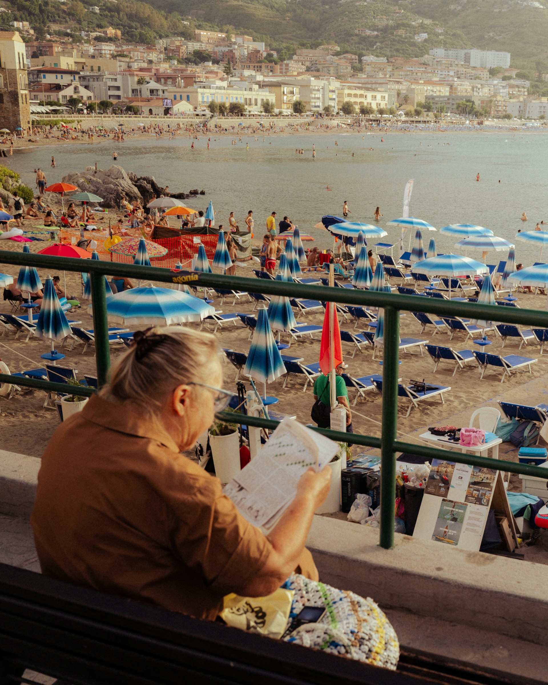 Woman reading on a bench overlooking a crowded beach